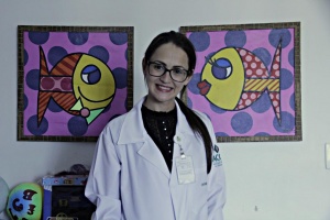 Enfermeira do hospital sorri à frente de parede com dois quadros coloridos