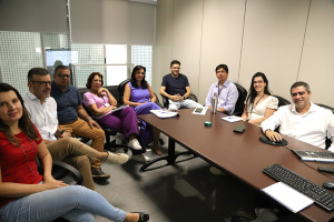 Várias pessoas sentadas numa mesa oval numa sala de reuniões