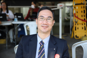 Foto do Advogado César durante campanha de doação de sangue. Trata-se de um homem amarelo, com cabelo curto, preto e liso. Ele está vestido de terno e óculos preto e posa sorrindo para a foto, de pé. 