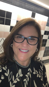 Close de mulher de óculos de grau, blusa preta com desenhos claros, Ela sorri.