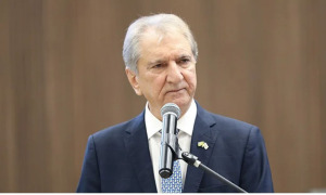 Homem grisalho de terno fala ao microfone