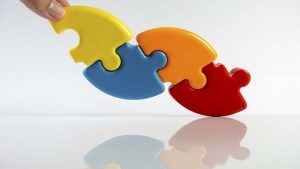 Hand holding multicolour pie chart or pieces of puzzle. Concept of process solution and teamwork collaboration. Isolated on white background. Slightly de-focused and close-up shot. Copy space.