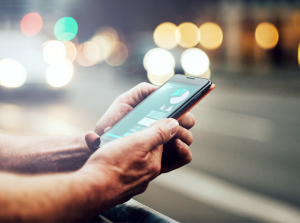 Foto colorida mostrando as mãos de um homem segurando um celular