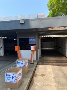 Foto da entrada do estacionamento do Fórum onde estão posicionadas duas caixas de papelão com cartazes colados com os dizeres "Doe brinquedos"