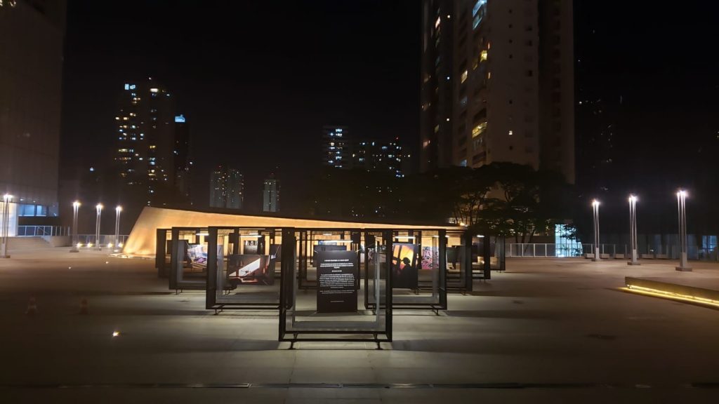 Foto mostra os paineis da exposição na praça em período noturno