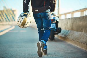 motoqueiro com capacete na mão caminhando rumo a sua moto