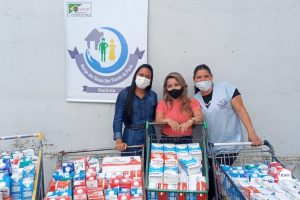 imagem mostra três mulheres com máscaras ao lado de centenas de litros de leites doados