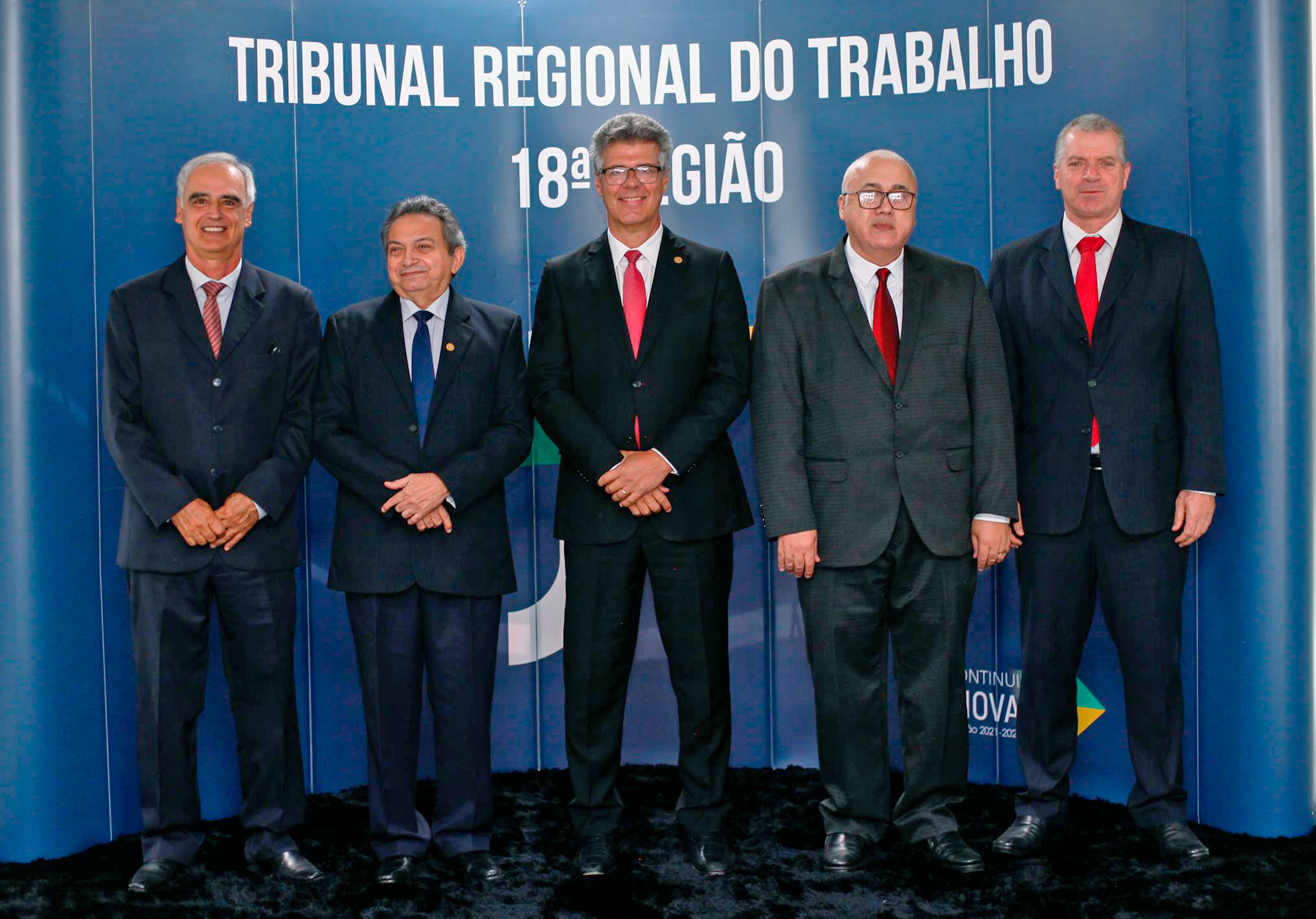 Foto de autoridades em pé em frente a um painel do TRT-18, conforme identificado na legenda da foto