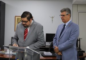 Foto colorida mostra o juiz Fabiano Coelho (à esquerda) assinando termo de assunção de titularidade da VT de Goiatuba. Ao lado dele o presidente do TRT-18