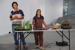 Um homem e uma mulher atrás de uma mesa com mudas e materiais para plantio