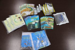 Kit para os estudantes com alcool em gel, cartilhas, cadernos, camisetas, máscaras e porta-trecos