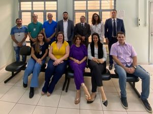 Cinco pessoas sentadas em cadeiras. Atrás delas, sete pessoas em pé, lado a lado