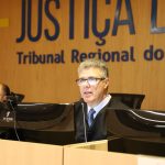 Desembargador Daniel Viana Junior, durante sessão plenária. Ele está sentado em frente a uma mesa com computador e microfone