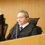 Desembargador Geraldo Rodrigues Nascimento, durante sessão plenária. Ele está sentado em frente a uma mesa com computador e microfone