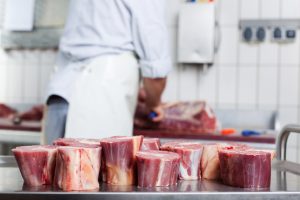 Um açogueiro ao fundo da imagem e alguns cortes de carne em primeiro plano