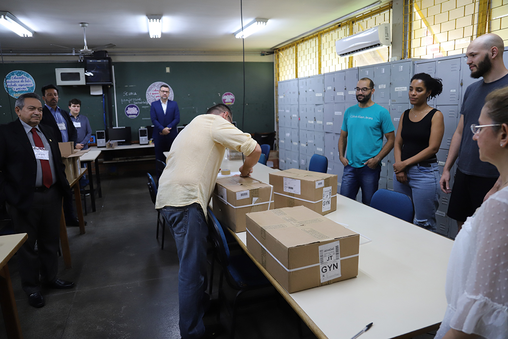 Integrantes da Comissão do Concurso acompanham abertura de caixas com provas, um homem abre as caixas enquanto outros observam