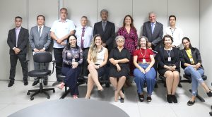 Foto mostra uma sala de audiência em que várias pessoas, umas sentadas e outras em pé, posam para foto
