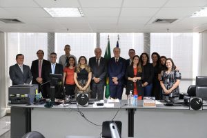 Pessoas em pé, atrás de uma mesa, posando para foto. São sete mulheres e sete homens. Todos estão sorrindo.