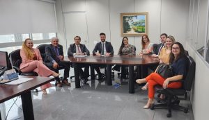 Mulheres e homens sentados ao redor de uma mesa de madeira. Todos estão sorrindo