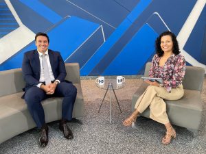 Duas pessoas, um homem e uma mulher, sentados com uma mesa ao centro.