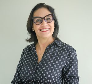 Foto da Juíza Wanda. Trata-se de uma mulher branca, com cabelos escuros à altura dos ombros. Na imagem, ela utiliza um óculos e uma blusa escura, enquanto sorri em direção à câmera.