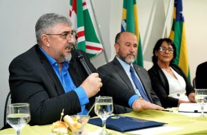 três pessoas na banca e uma falando ao microfone