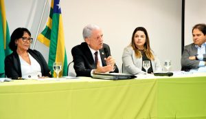 Quatro pessoas numa bancada sendo um homem com microfone a falar