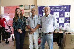 Foto da esquerda para a direita, da Lara Nercessian, do Manoel Silva e do Crebilon de Araújo. Os 3 estão de pé, posando lado a lado, em frente a uma mesa cheia de doações.