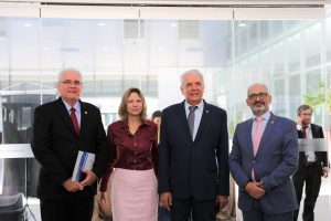 Foto de magistrados e palestrante durante evento. Tratam-se de 3 homens e 1 mulher, estão todos de pé, alinhados lado a lado e posando para a foto.