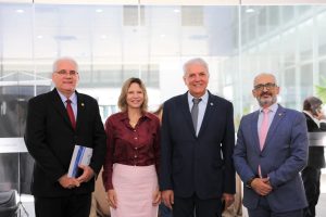 Foto de magistrados e palestrante durante evento. Tratam-se de 3 homens e 1 mulher, estão todos de pé, alinhados lado a lado e posando para a foto.
