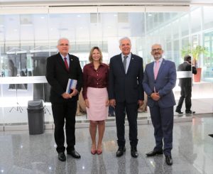 Foto de magistrados e palestrante durante evento. Tratam-se de 3 homens e 1 mulher, estão todos de pé, alinhados lado a lado e posando para a foto.