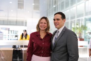 Foto de um juiz e de uma palestrante durante evento. Os dois posam lado a lado e sorriem para a foto.