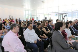 Foto de plateia do evento. As pessoas estão sentadas em cadeiras alinhadas horizontalmente e verticalmente.
