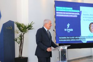 Foto do desembargador Eugênio Cesário discursando durante evento. Trata-se de um homem branco, de cabelo curto, liso e grisalho. Ele veste terno preto e gravata cinza. O homem está atrás de um púlpito e fala no microfone de mesa.