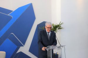 Foto do desembargador Eugênio Cesário discursando durante evento. Trata-se de um homem branco, de cabelo curto, liso e grisalho. Ele veste terno preto, gravata cinza e óculos de armação preta. O homem está atrás de um púlpito e fala no microfone de mesa.