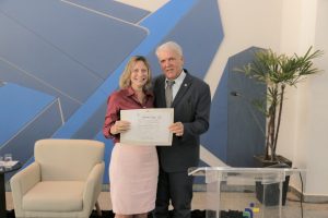 Foto de desembargador Eugênio Cesário com uma palestrante durante evento. Os dois estão lado a lado e seguram juntos um certificado.