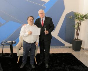 Foto de desembargador Wellington Peixoto com palestrante. Os dois estão de pé, lado a lado, e posam para a foto. O desembargador segura um microfone de mão e o palestrante segura um certificado.