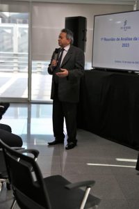 Desembargador Geraldo Nascimento discursando na reunião estratégica. Trata-se de um homem branco, de cabelo curto, liso e grisalho. Ele veste terno e gravata pretos. Está de pé, em frente a uma televisão falando no microfone.