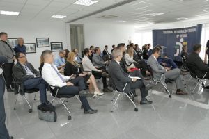 Foto de servidores e servidoras na Reunião Estratégica. A imagem mostra os participantes de uma vista diagonal, sentados em cadeiras organizadas em fileiras
