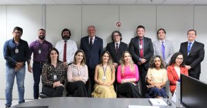 Foto da equipe da 3ª Vara do Trabalho com o desembargador Eugênio Cesário. Na imagem há 8 homens de pé. alinhados lado a lado. Na frente dos homens, há 6 mulheres sentadas em cadeiras posicionadas lado a lado.