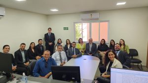 Foto do Corregedor-regional, desembargador Eugênio Cesário, com advogados durante audiência pública. Na imagem, um grupo de pessoas está sentado ao redor de uma mesa enquanto outro grupo de pessoas senta em cadeiras dispostas ao redor da sala branca. 