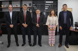 Cinco pessoas em pé numa sala, sendo quatro homens e uma mulher, em pose para foto. Atrás uma estante.