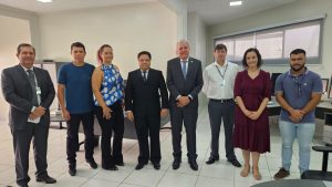 Oito pessoas em pé dentro de uma sala, com paredes de cor bege, sendo duas mulheres e seis homens. Eles posam para foto