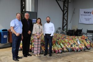 Em primeiro plano, três homens e uma mulher. Em segundo plano, organizadas no chão, há 397 cestas de hortifrutis para doação