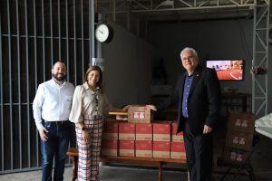 Dois homens e uma mulher de pé ao lado de caixas de leite. Eles estão sorrindo e posando para a foto