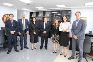 Foto colorida mostrando sete pessoas de pé, lado a lado. Tratam-se de três mulheres e quatro homens usando roupas formais e sorrindo enquanto posam para foto