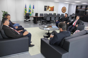 Várias pessoas sentadas numa sala com uma mesa ao fundo