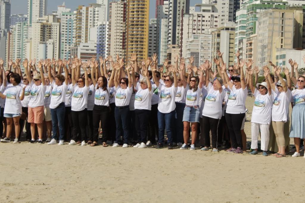 Foto de todo o coral reunido em um grande grupo, estão todos com os braços levantados e olhando para frente.