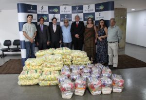 Foto colorida dos representantes do TRT e das associações atrás dos alimentos doados. Tratam-se de 6 homens e 2 mulheres, estão de pé e se posicionam lado a lado para tirar a foto.