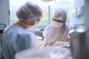 Foto colorida mostrando uma dentista e uma estagiária de saúde bucal realizando atendimento odontológico